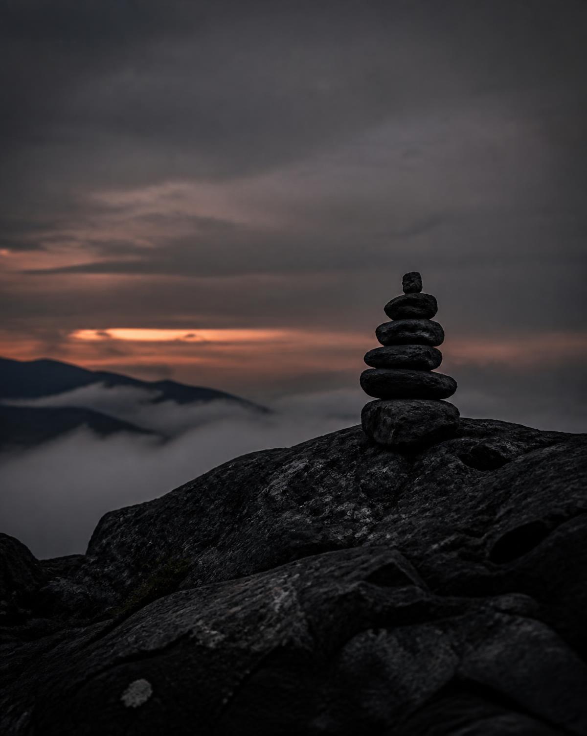 A stacked stone cairn marking a path on a dark ridge above the fog